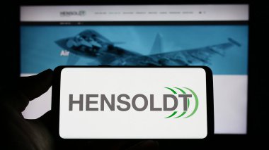 Stuttgart, Germany - 04-21-2023: Person holding cellphone with logo of German defense company Hensoldt AG on screen in front of business webpage. Focus on phone display. clipart