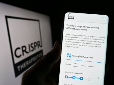 Stuttgart, Almanya - 04-21-2023: Biyoteknoloji şirketi CRISPR Therapeutics 'in web sayfası ile cep telefonu tutan kişi logolu ekranda. Telefon ekranının merkezine odaklan.