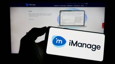 Stuttgart, Almanya - 04-23-2023: Amerikan yazılım şirketi iManage LLC 'nin logosuna sahip cep telefonu sahibi kişi iş sayfasının önünde ekranda. Telefon ekranına odaklan.