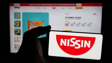 Stuttgart, Almanya - 01-14-2025: Japon şirketi Nissin Foods Holding Co. Ltd. nin logosuyla cep telefonu sahibi kişi web sayfasının önünde ekranda. Telefon ekranına odaklan.