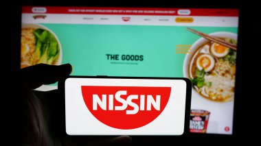 Stuttgart, Almanya - 01-14-2025: Japon şirketi Nissin Foods Holding Co. Ltd. nin logosuyla cep telefonu sahibi kişi web sayfasının önünde ekranda. Telefon ekranına odaklan.