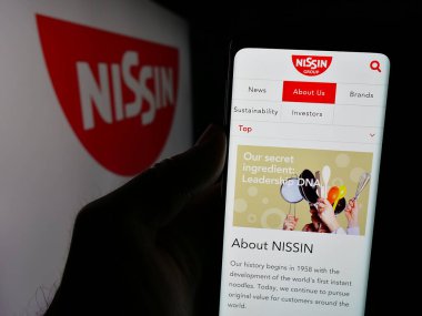 Stuttgart, Almanya - 01-14-2025: Japon şirketi Nissin Foods Holding Co. Ltd. nin internet sayfası ile cep telefonu tutan kişi logo ile ekranda. Telefon ekranının merkezine odaklan.