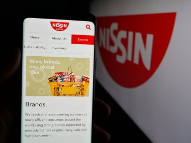 Stuttgart, Almanya - 01-14-2025: Japon şirketi Nissin Gıda Holding Co. Ltd. nin internet sayfası ile akıllı telefon sahibi kişi logo ile ekranda. Telefon ekranının merkezine odaklan.