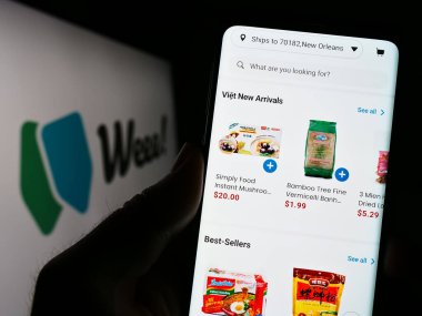 Stuttgart, Almanya - 03-28-2023: ABD market dağıtım şirketi Weee Inc. 'in web sayfası ile cep telefonu tutan kişi logolu ekranda. (Sayweee) Telefon ekranının merkezine odaklan.