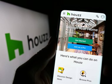 Stuttgart, Germany - 03-28-2023: Person holding cellphone with webpage of interior design platform company Houzz Inc. on screen in front of logo. Focus on center of phone display. clipart