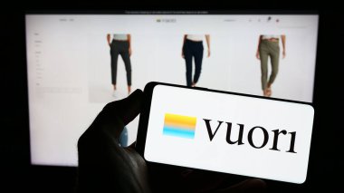 Stuttgart, Almanya - 03-30-2023: Üzerinde ABD 'li giyim şirketi Vuori Inc.' nin logosu olan cep telefonu sahibi kişi iş sayfasının önünde ekranda. Telefon ekranına odaklan.