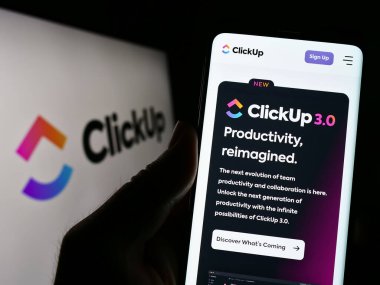 Stuttgart, Almanya - 03-30-2023: ABD 'li Mango Technologies Inc. (ClickUp) şirketinin web sayfası ile cep telefonu tutan kişi logo ile ekranda. Telefon ekranının merkezine odaklan.