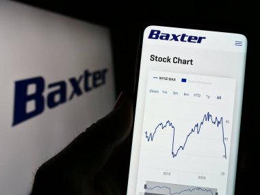 Stuttgart, Almanya - 03-31-2023: ABD 'li sağlık şirketi Baxter International Inc.' in internet sayfası ile cep telefonu tutan kişi logolu ekranda. Telefon ekranının merkezine odaklan.