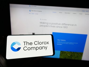 Stuttgart, Germany - 03-31-2023: Person holding mobile phone with logo of American chemicals manufacturer Clorox Company on screen in front of web page. Focus on phone display. clipart