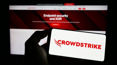 Stuttgart, Almanya - 03-31-2023: İnternet sitesi önünde üzerinde siber güvenlik şirketi CrowdStrike Holding Inc. 'nin logosu bulunan akıllı telefon sahibi kişi. Telefon ekranına odaklan.
