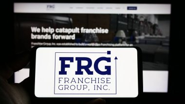 Stuttgart, Almanya - 03-31-2023: ABD 'li Franchise Group Inc. (FRG) şirketinin logosunun bulunduğu cep telefonu sahibi kişi iş sayfası önünde ekranda. Telefon ekranına odaklan.