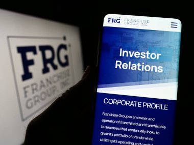 Stuttgart, Almanya - 03-31-2023: ABD 'li Franchise Group Inc. (FRG) şirketinin web sayfası logonun önünde bulunan kişi. Telefon ekranının merkezine odaklan.