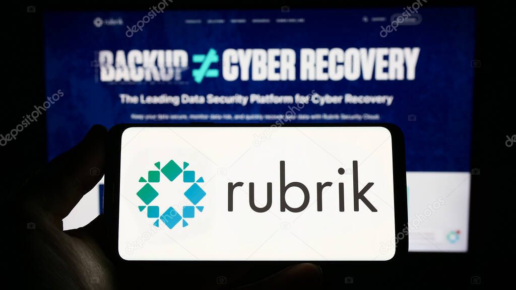 Stuttgart, Germany - 03-30-2023: Person holding smartphone with logo of US data security company Rubrik Inc. on screen in front of website. Focus on phone display.