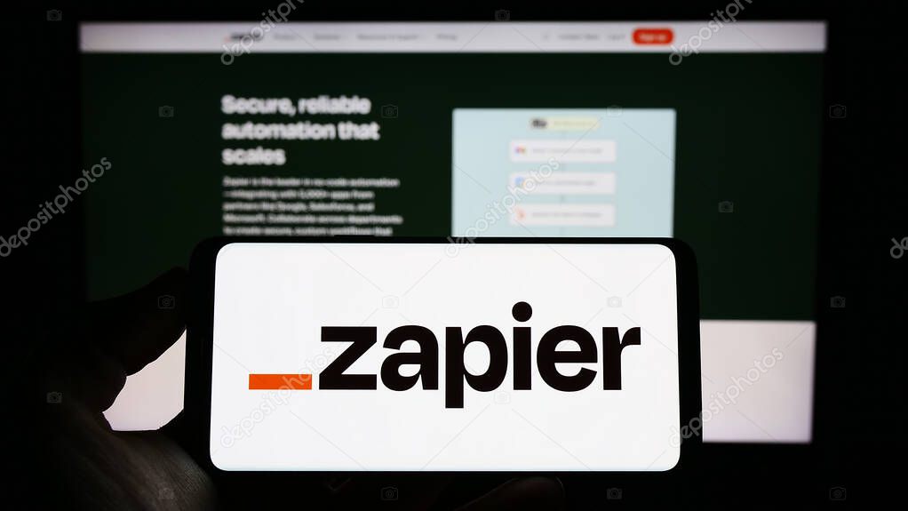 Stuttgart, Germany - 03-30-2023: Person holding cellphone with logo of US automation software company Zapier Inc. on screen in front of business webpage. Focus on phone display.