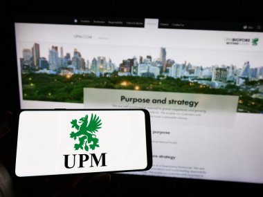 Stuttgart, Germany - 03-31-2023: Person holding mobile phone with logo of Finnish forestry company UPM-Kymmene Oyj on screen in front of business web page. Focus on phone display. clipart