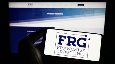 Stuttgart, Almanya - 03-31-2023: İnternet sitesi önünde üzerinde ABD 'li Franchise Group Inc. (FRG) şirketinin logosu bulunan akıllı telefon sahibi kişi. Telefon ekranına odaklan.