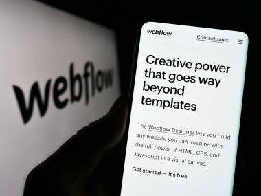 Stuttgart, Almanya - 03-31-2023: ABD 'li web geliştirme yazılım şirketi Webflow Inc.' in web sayfası ile cep telefonu tutan kişi logolu ekranda. Telefon ekranının merkezine odaklan.