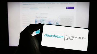 Stuttgart, Almanya - 04-01-2023: Clearstream International SA şirketinin logosuyla cep telefonu sahibi kişi iş sayfasının önünde ekranda. Telefon ekranına odaklan.