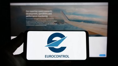 Stuttgart, Almanya - 04-01-2023: Web sitesi önünde ekranda hava trafik yönetim kuruluşu Eurocontrol 'un logosuna sahip akıllı telefonu tutan kişi. Telefon ekranına odaklan.