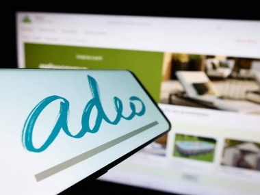 Stuttgart, Almanya - 04-01-2023: Fransız perakende şirketi Adeo SA 'nın logosuna sahip akıllı telefon, iş dünyasının web sitesinin önünde ekranda. Telefon ekranının merkez soluna odaklan.