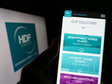 Stuttgart, Almanya - 04-01-2023: Fransız hidrojen şirketi HDF Energy 'nin web sitesiyle birlikte logo önünde akıllı telefon tutan kişi. Telefon ekranının merkezine odaklan.