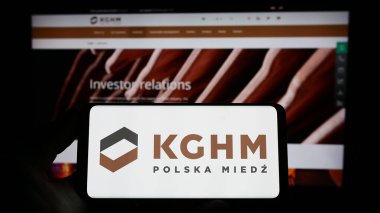 Stuttgart, Germany - 04-01-2023: Person holding smartphone with logo of Polish mining company KGHM Polska Miedz S.A. on screen in front of website. Focus on phone display. clipart