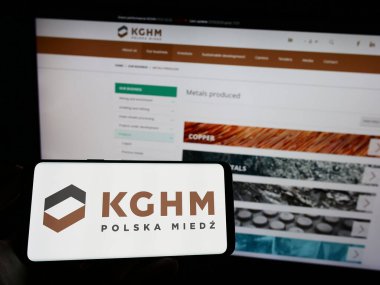 Stuttgart, Germany - 04-01-2023: Person holding mobile phone with logo of Polish mining company KGHM Polska Miedz S.A. on screen in front of web page. Focus on phone display. clipart