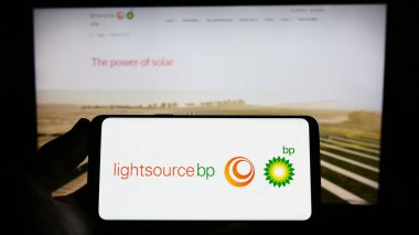 Stuttgart, Germany - 04-01-2023: Person holding smartphone with logo of British renewable energy company Lightsource BP on screen in front of website. Focus on phone display. clipart