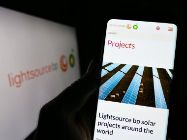 Stuttgart, Germany - 04-01-2023: Person holding smartphone with web page of British renewable energy company Lightsource BP on screen with logo. Focus on center of phone display. clipart