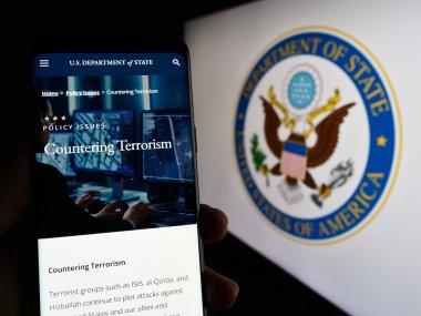 Stuttgart, Germany - 04-01-2023: Person holding smartphone with webpage of United States Department of State (DOS) on screen in front of logo. Focus on center of phone display. clipart