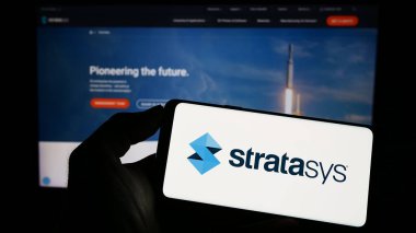 Stuttgart, Almanya - 04-01-2023: Üzerinde 3D baskı şirketi Stratasys Ltd. 'nin logosu olan cep telefonu sahibi kişi iş sayfasının önünde ekranda. Telefon ekranına odaklan.
