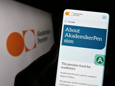 Stuttgart, Germany - 04-01-2023: Person holding cellphone with webpage of Danish pension fund AkademikerPension on screen in front of logo. Focus on center of phone display. clipart