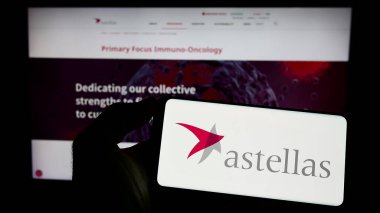 Stuttgart, Almanya - 04-01-2023: İnternet sitesi önünde üzerinde Astellas İlaç Şirketi logosu olan akıllı telefon sahibi kişi. Telefon ekranına odaklan.