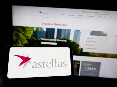 Stuttgart, Almanya - 04-01-2023: İnternet sayfası önünde üzerinde ilaç şirketi Astellas Pharma Inc. 'in logosu bulunan cep telefonu sahibi kişi. Telefon ekranına odaklan.