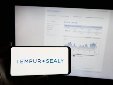 Stuttgart, Germany - 01-15-2025: Person holding smartphone with logo of US bedding company Tempur Sealy International Inc. on screen in front of website. Focus on phone display. clipart