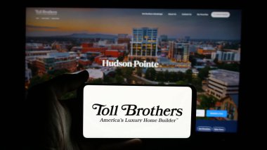 Stuttgart, Almanya - 01-15-2025: ABD 'li ev yapımı şirketi Toll Brothers Inc.' in logosuyla cep telefonu sahibi kişi iş sayfasının önünde ekranda. Telefon ekranına odaklan.