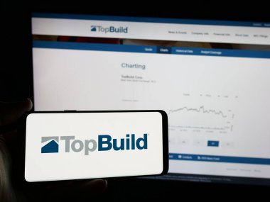 Stuttgart, Almanya - 01-15-2025: ABD 'li inşaat malzemeleri şirketi TopBuild Corp' un logosunu elinde tutan kişi web sitesinin önünde ekranda. Telefon ekranına odaklan.