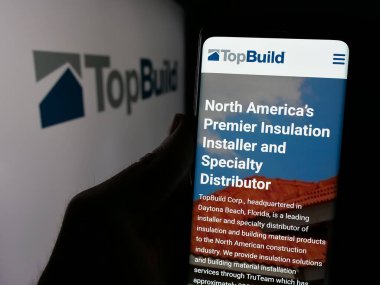Stuttgart, Almanya - 01-15-2025: ABD 'li inşaat malzemeleri şirketi TopBuild Corp' un web sitesi ile cep telefonu tutan kişi logonun önünde ekranda. Telefon ekranının merkezine odaklan.