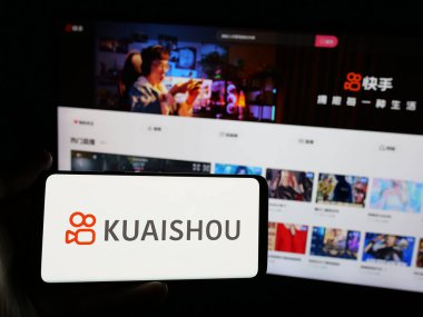 Stuttgart, Almanya - 01-16-2025: Çinli video paylaşım uygulaması şirketi Kuaishou 'nun logosuna sahip akıllı telefon sahibi kişi web sitesinin önünde ekranda. Telefon ekranına odaklan.