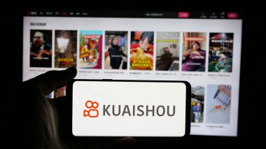 Stuttgart, Almanya - 01-16-2025: Çinli video paylaşım uygulaması şirketi Kuaishou 'nun logosuyla cep telefonu sahibi kişi iş sayfasının önünde ekranda. Telefon ekranına odaklan.