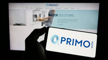 Stuttgart, Almanya - 03-22-2023: ABD 'li Primo Water Corporation şirketinin logosuyla cep telefonu sahibi kişi iş sayfasının önünde ekranda. Telefon ekranına odaklan.