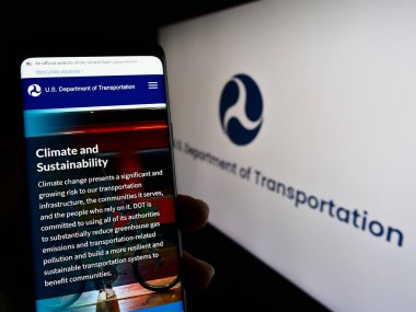 Stuttgart, Almanya - 03-22-2023: ABD Ulaştırma Bakanlığı 'nın (USDOT) web sayfası ile ekranda logolu cep telefonu tutan kişi. Telefon ekranının merkezine odaklan.