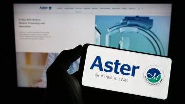Stuttgart, Almanya - 03-22-2023: Sağlık şirketi Aster DM Healthcare Limited 'in logosuyla cep telefonu sahibi kişi iş sayfası önünde ekranda. Telefon ekranına odaklan.