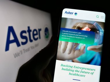 Stuttgart, Almanya - 03-22-2023: Sağlık şirketi Aster DM Healthcare Limited 'in internet sayfası ile cep telefonu tutan kişi logo önünde ekranda. Telefon ekranının merkezine odaklan.