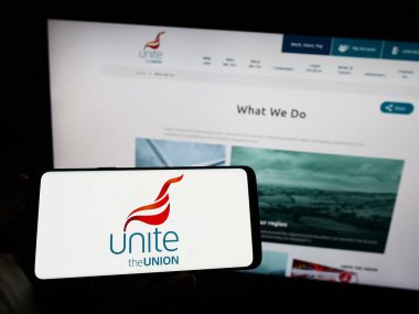 Stuttgart, Almanya - 03-22-2023: İngiliz Sendikası logosuyla cep telefonu tutan kişi web sayfası önünde Birliği Birleştirin. Telefon ekranına odaklan.