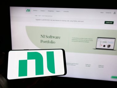 Stuttgart, Almanya - 03-23-2023: Web sayfası önünde National Instruments Corporation (NI) şirketinin logosuna sahip cep telefonu sahibi kişi. Telefon ekranına odaklan.
