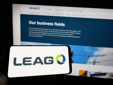 Stuttgart, Germany - 03-23-2023: Person holding mobile phone with logo of German energy company LEAG on screen in front of business web page. Focus on phone display. clipart