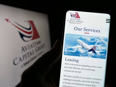 Stuttgart, Almanya - 03-24-2023: ABD 'li kiralama şirketi Aviation Capital Group LLC' nin web sayfası ile cep telefonu tutan kişi logolu ekranda. Telefon ekranının merkezine odaklan.