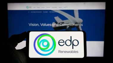 Stuttgart, Germany - 03-24-2023: Person holding cellphone with logo of Spanish energy company EDP Renovaveis S.A. (EDPR) on screen in front of webpage. Focus on phone display. clipart