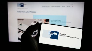 Stuttgart, Almanya - 03-24-2023: Web sayfası önünde üzerinde Deutsche Industri- und Handelskammer (DIHK) logosu bulunan kişi. Telefon ekranına odaklan.